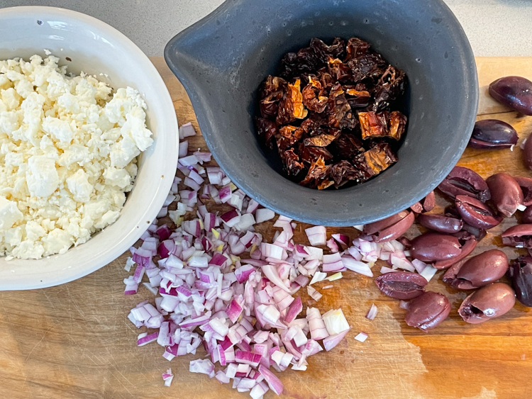 rödlök, fetaost, soltorkade tomater och oliver på skärbräda